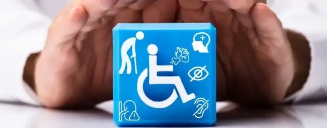 Dłonie obejmujące niebieski sześcian z symbolem osoby na wózku oraz ikonami oznaczającymi różne rodzaje niepełnosprawności, m.in. wzrokową, słuchową, ruchową i intelektualną.